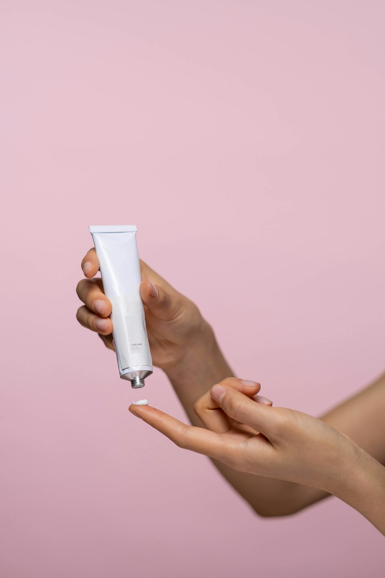 Hand squeezing white azelaic acid cream tube into palm for hyperpigmentation rosacea and acne