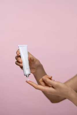 Person dispensing tretinoin cream from a white tube onto their hand