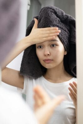 Woman examining her face in the mirror checking for dark spots and pigmentation