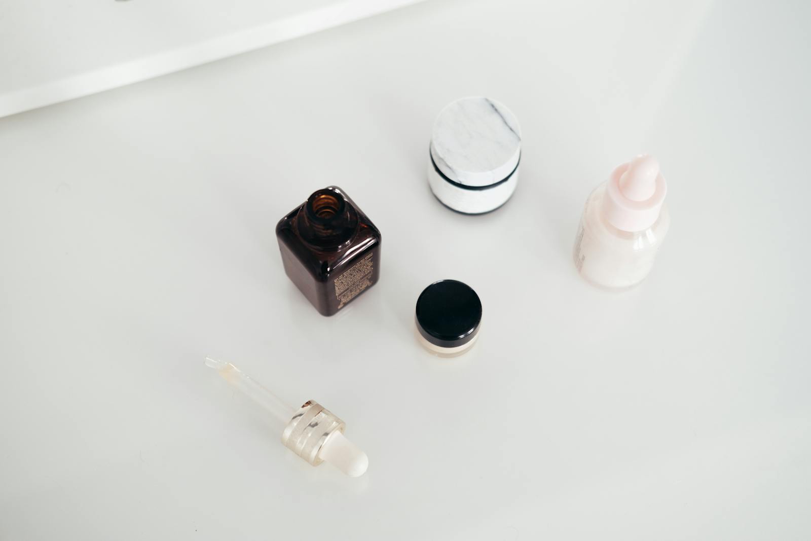 Flat lay of skincare serum, cream jar and dropper representing kojic acid product formats