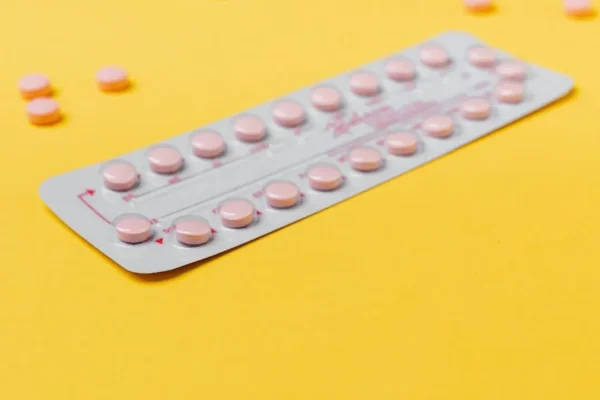 Pink contraceptive pills on a yellow surface