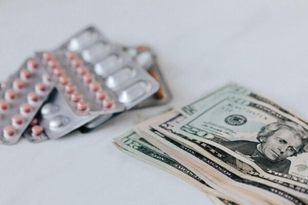 Brand-name medication blister packs next to US dollar bills, illustrating the price gap between branded and WHO-GMP generic medications