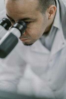 Scientist in lab coat examining samples through microscope — CJC-1295 research