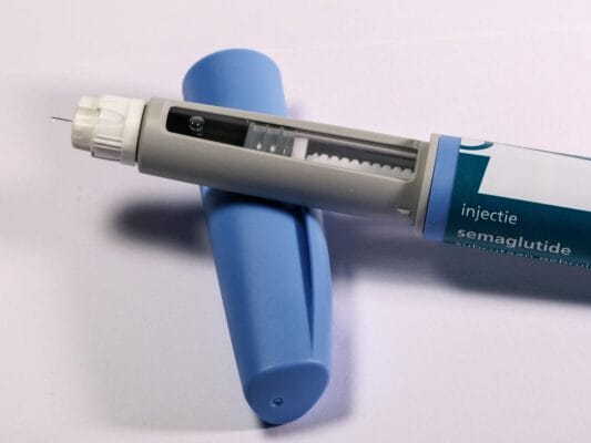 Semaglutide injection pen alongside its cap on a neutral background, illustrating the brand-versus-compounded format that defines the Ozempic comparison