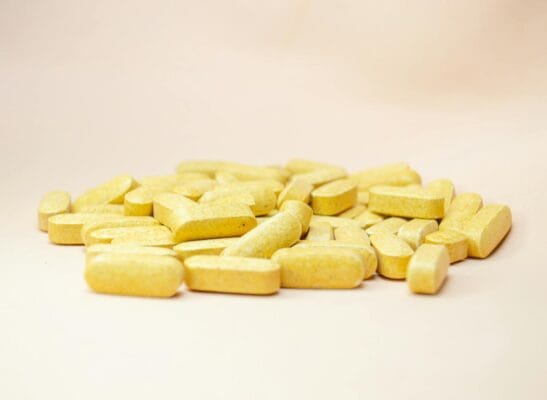 Yellow tadalafil-style oval tablets piled on a neutral background, illustrating the daily vs on-demand dosing decision for ED and BPH