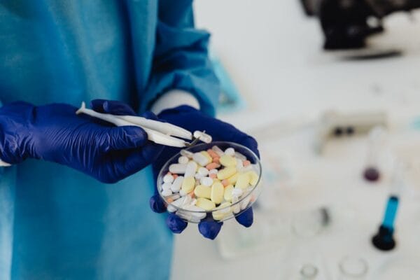 Scientist in gloves handling pills in a petri dish representing antiparasitic drug cancer research