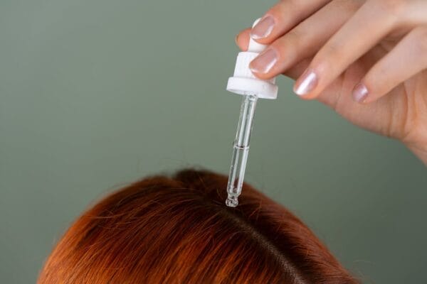Close-up of applying copper peptide hair serum with precision dropper to hair roots