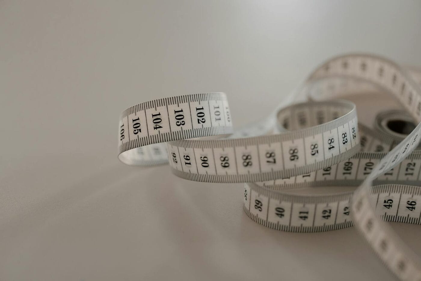 Soft white tape measure loosely coiled on a neutral surface — GLP-1 plateau and month 4 weight loss stall on Ozempic, Wegovy or Mounjaro