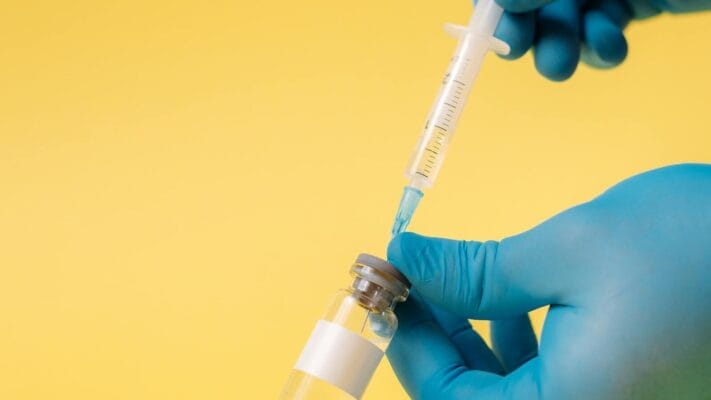 Gloved hands holding syringe and vial demonstrating HCG reconstitution