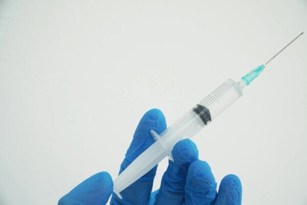 Gloved hands holding a medical syringe for Hynidase injection (hyaluronidase) administration