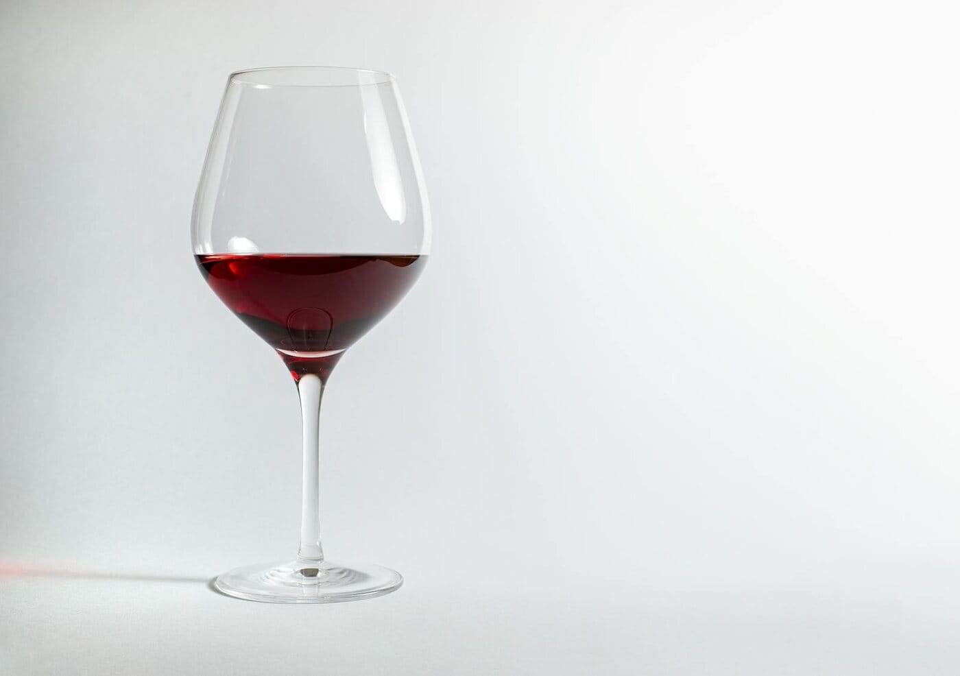 Red wine glass less than half full on a white background — Ozempic and alcohol, why tolerance changes on GLP-1 medication