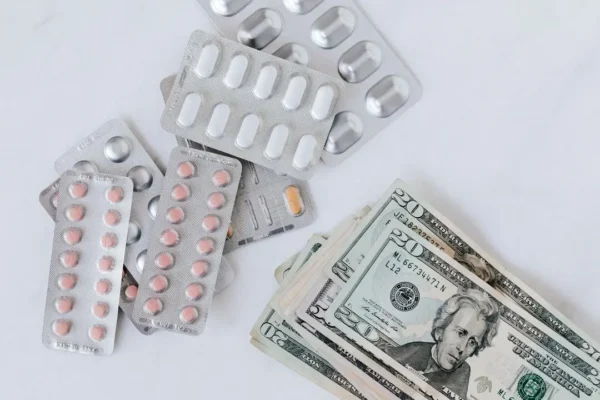 Blister-pack pills next to US dollar banknotes — medication cost concept