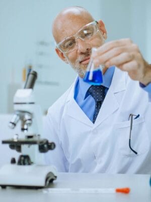 Scientist in lab coat with blue liquid in flask — GHRH research
