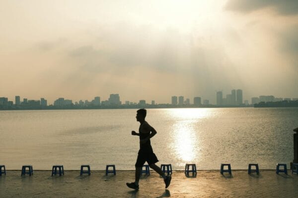 Runner silhouetted against golden lakeside sunrise, signalling vigor and vitality the way mitochondrial peptides target cellular energy
