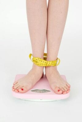 Measuring tape around legs on scale — weight-loss research