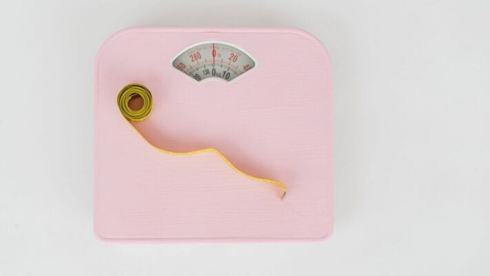 Pink bathroom weighing scale with a measuring tape, illustrating IUD and weight gain concerns